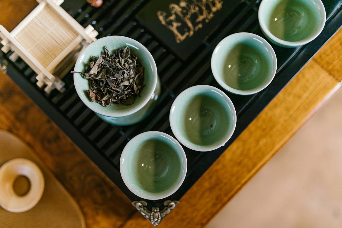 Green tea set on a wooden tray with four empty cups and a bowl of dried tea leaves, evoking a serene and traditional atmosphere.
