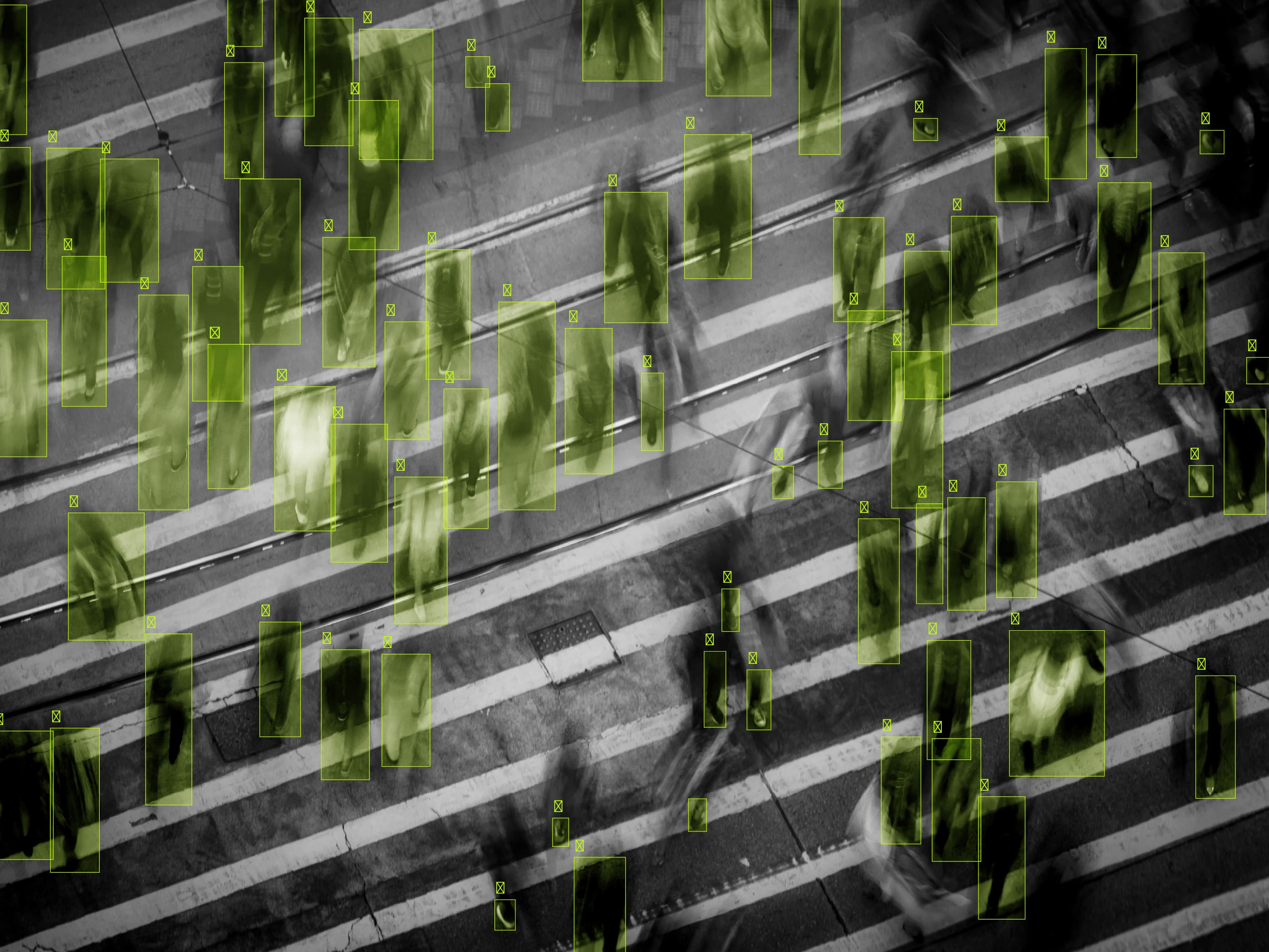 Overhead view of a busy crosswalk filled with blurred pedestrians. Green rectangles and numbers overlay the scene, conveying data tracking or AI detection.